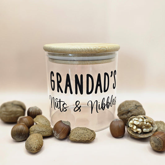 Jar labeled 'Grandad's Nuts & Nibbles' surrounded by nuts on a light background
