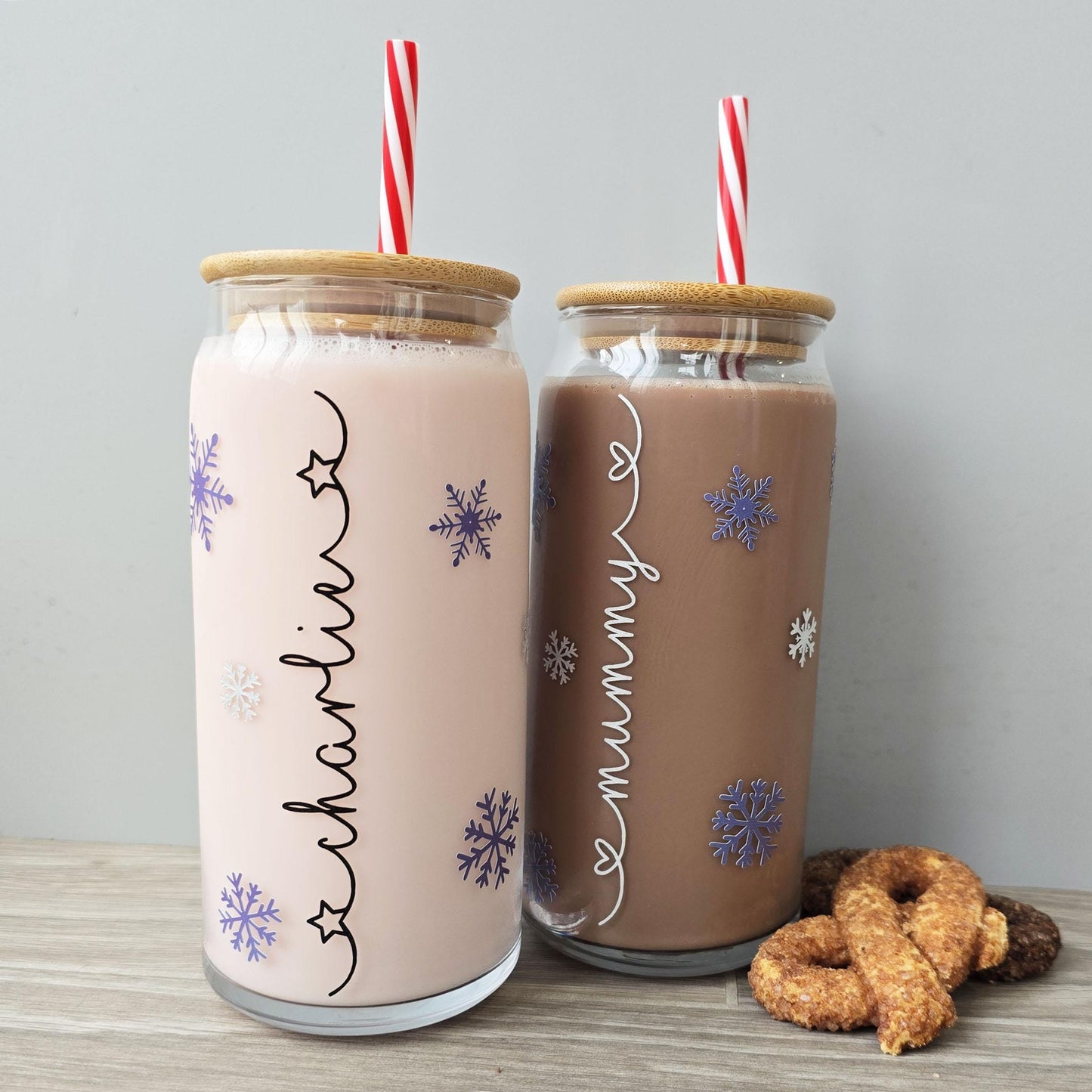 Personalised glass can drink holder with a bamboo suction lid and red and white reusable straw. Features silver snowflakes and blue snowflakes that colour change to purple when cold liquid is added to the glass. Personalised name along the side of the glass, available in glittery silver or black and features either a heart or stars at either end of the name.