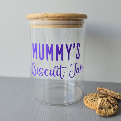 Clear jar with wooden lid labeled 'Mummy's Biscuit Jar' on a gray surface with cookies.