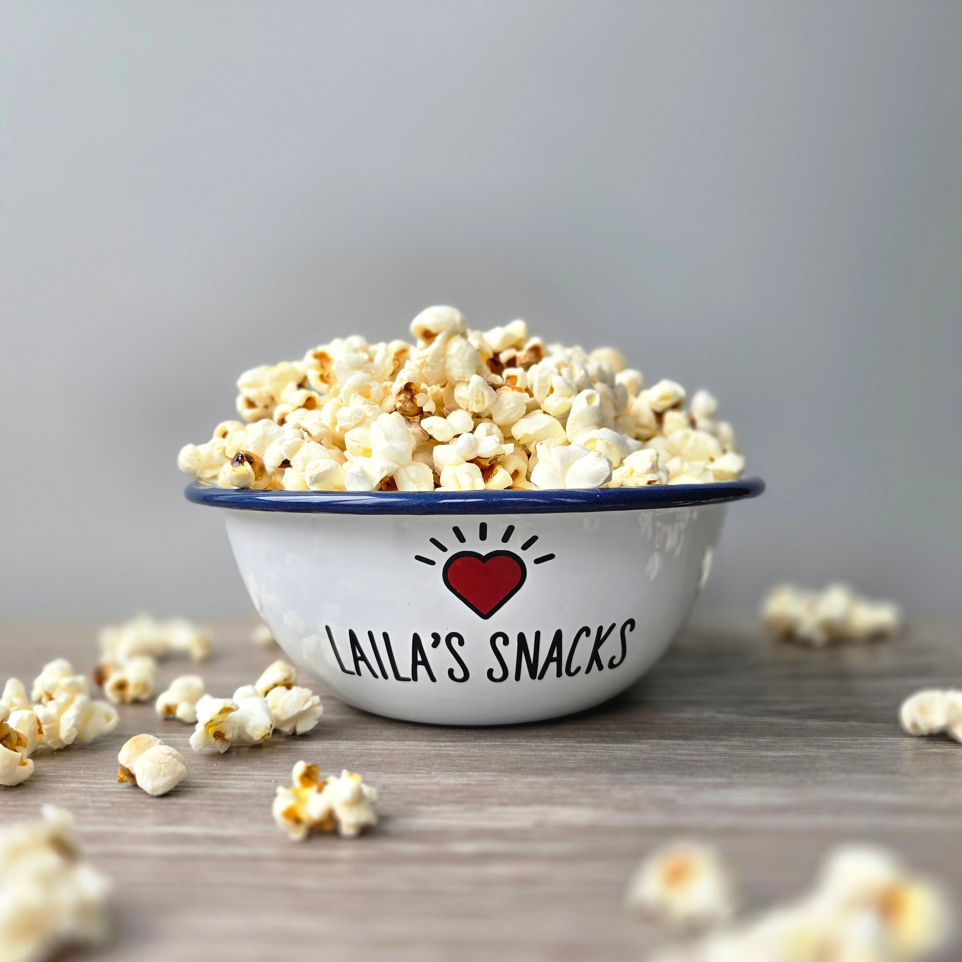 Kids Personalised white metal enamel snack bowl. White enamel metal bowl with navy blue rim. Printed with a yellow star or red heart and a name with snacks written underneath. Perfect for popcorn, sweets, crisps or general snacks.