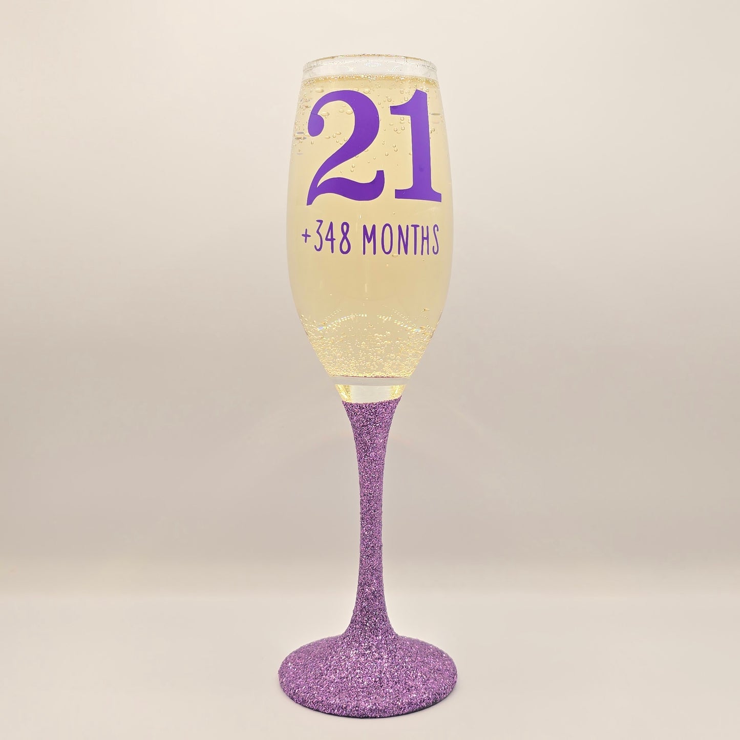 Prosecco glass or Champagne flute decorated with high shine glitter stem and personalised with 21 + the number of months to make up a 30th, 40th, 50th, 60th or 70th Birthday.