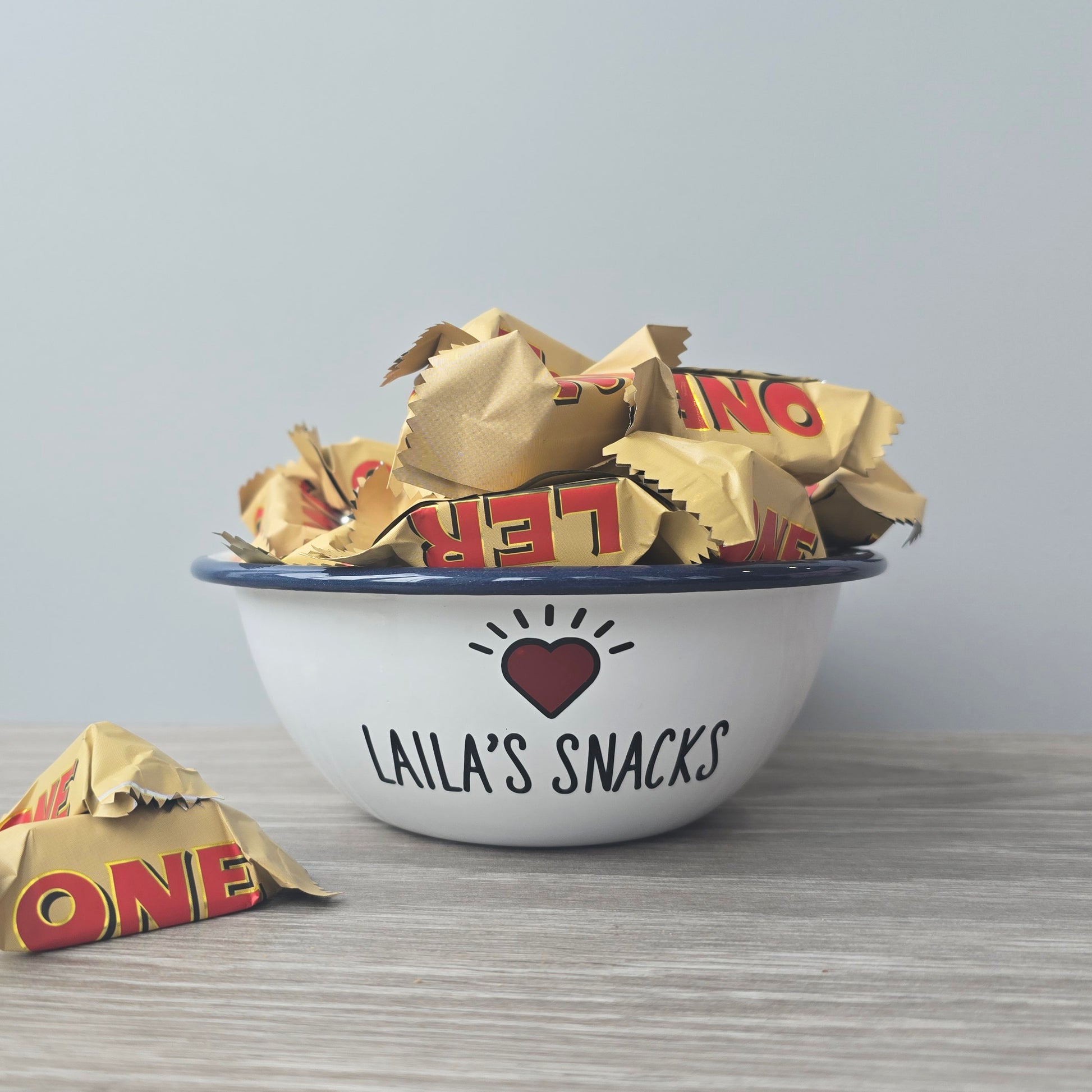 Kids Personalised white metal enamel snack bowl. White enamel metal bowl with navy blue rim. Printed with a yellow star or red heart and a name with snacks written underneath. Perfect for popcorn, sweets, crisps or general snacks.