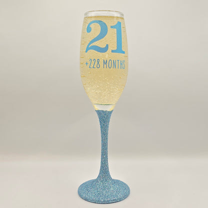 Prosecco glass or Champagne flute decorated with high shine glitter stem and personalised with 21 + the number of months to make up a 30th, 40th, 50th, 60th or 70th Birthday.