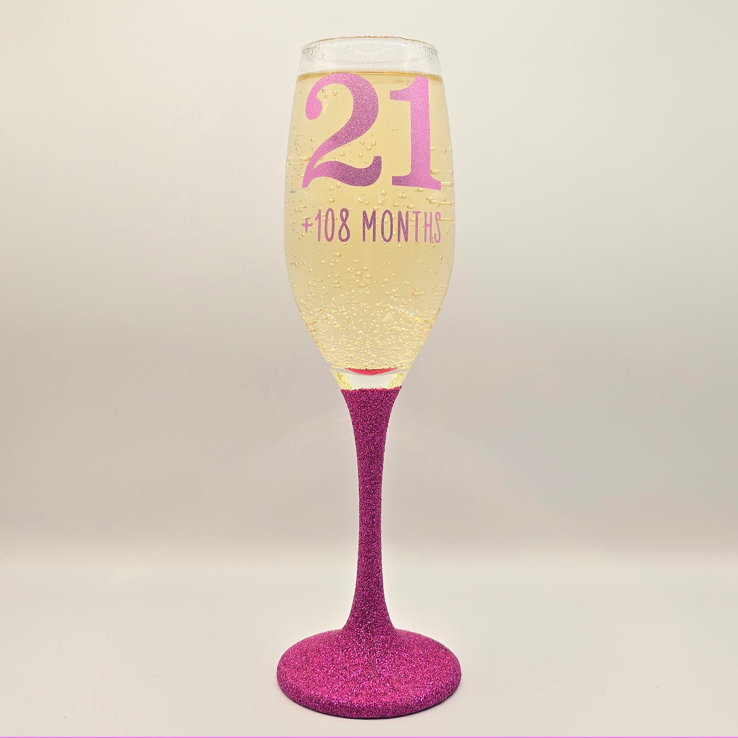 Prosecco glass or Champagne flute decorated with high shine glitter stem and personalised with 21 + the number of months to make up a 30th, 40th, 50th, 60th or 70th Birthday.
