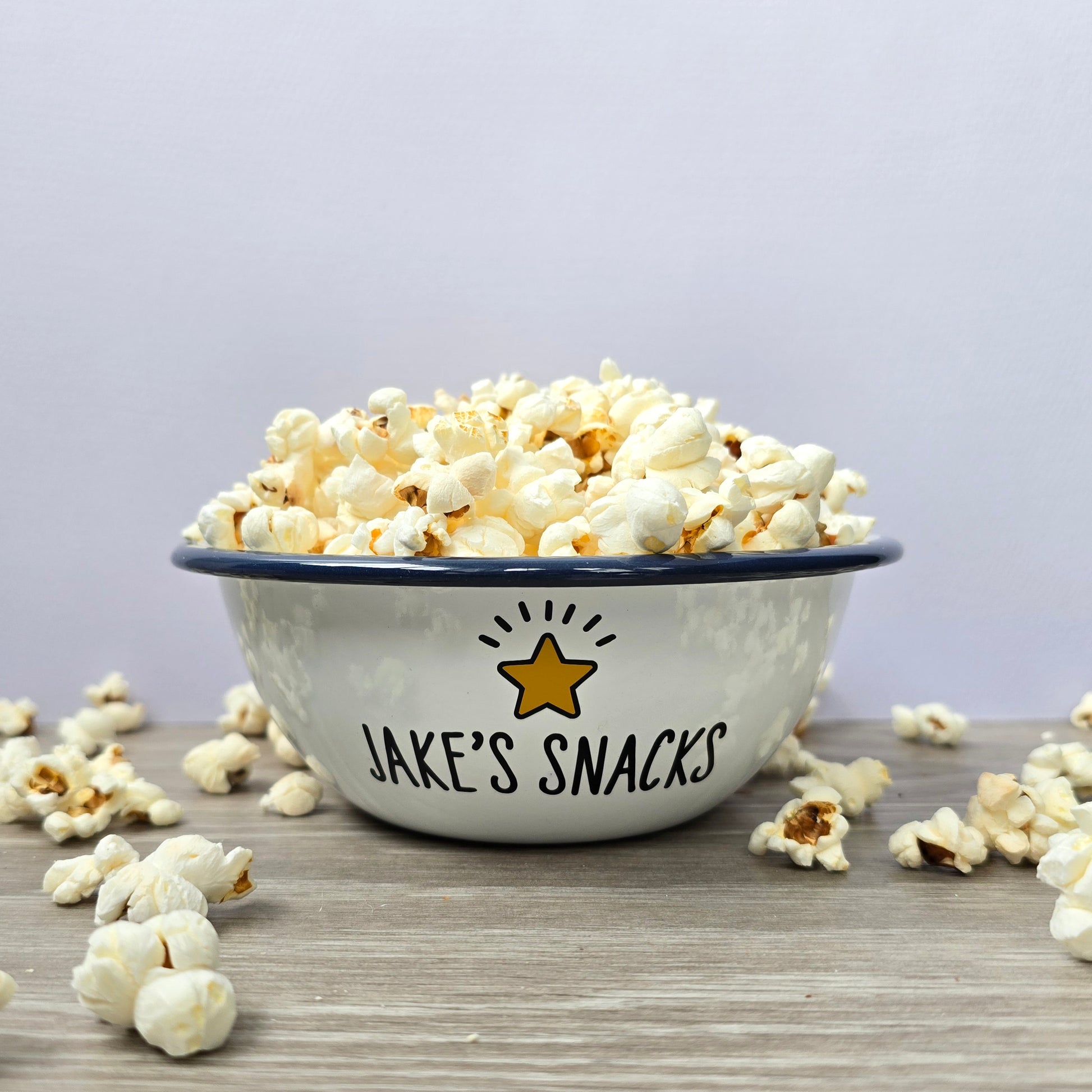 Kids Personalised white metal enamel snack bowl. White enamel metal bowl with navy blue rim. Printed with a yellow star or red heart and a name with snacks written underneath. Perfect for popcorn, sweets, crisps or general snacks.