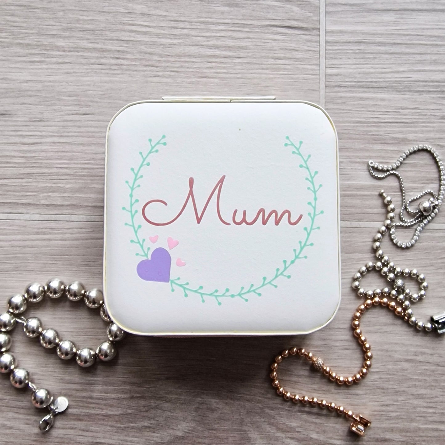 Faux leather, travel jewellery box personalised with a name in the middle of a decorative circle, decorated with hearts. Travel size jewellery case with zip and internal jewellery dividers.