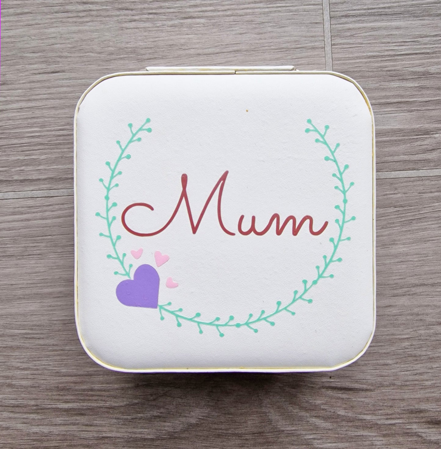 Faux leather, travel jewellery box personalised with a name in the middle of a decorative circle, decorated with hearts. Travel size jewellery case with zip and internal jewellery dividers.