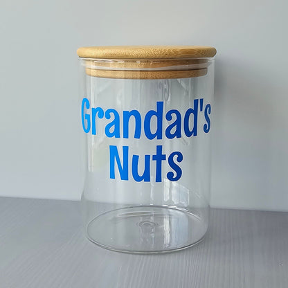 Personalised glass jar with wooden suction lids and blue text 'Grandad's Nuts' on a grey surface.