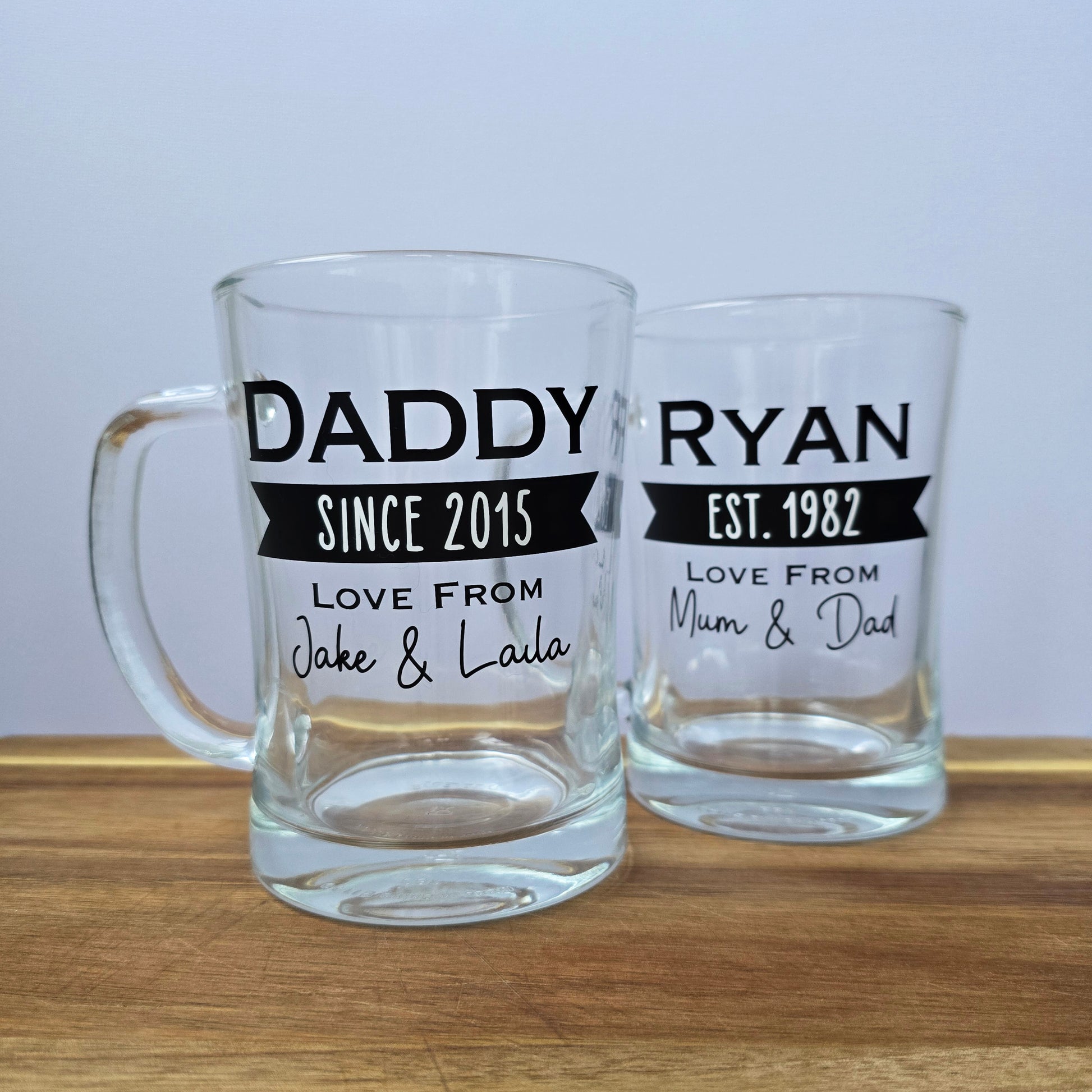 Glass beer tankard personalised with a name, year and signed from the gift giver in black vinyl on clear glass. Sturdy, heavy, clear glass stein with mixed font design. 