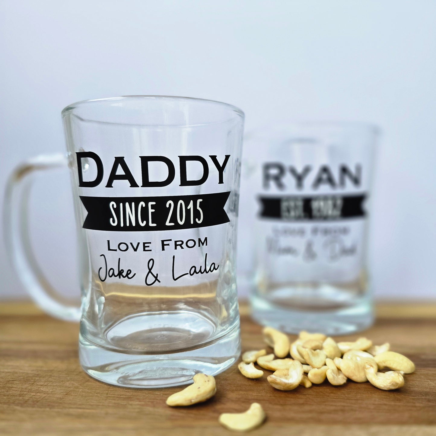 Glass beer tankard personalised with a name, year and signed from the gift giver in black vinyl on clear glass. Sturdy, heavy, clear glass stein with mixed font design. 