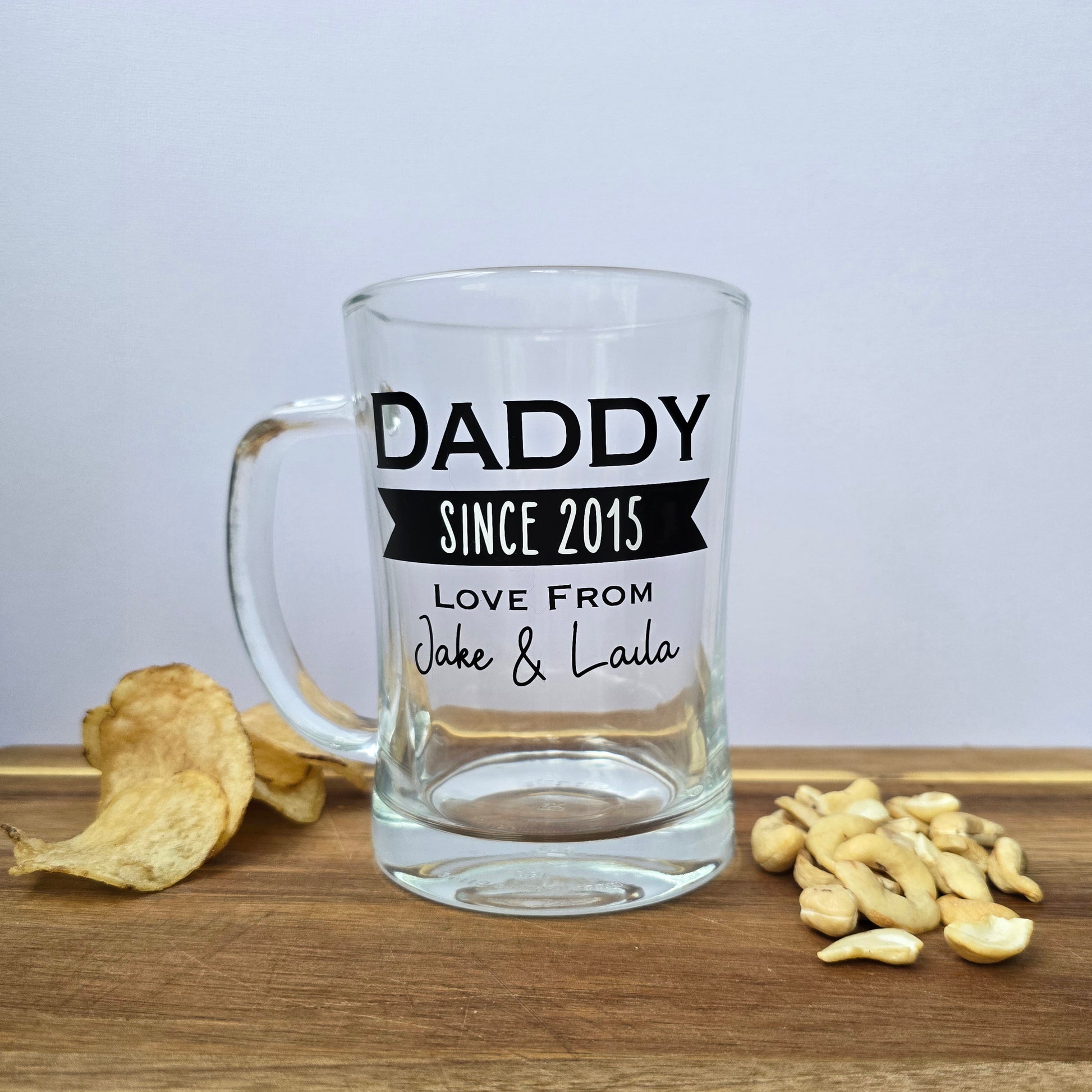 Glass beer tankard personalised with a name, year and signed from the gift giver in black vinyl on clear glass. Sturdy, heavy, clear glass stein with mixed font design. 