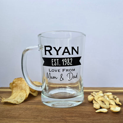 Glass beer tankard personalised with a name, year and signed from the gift giver in black vinyl on clear glass. Sturdy, heavy, clear glass stein with mixed font design. 