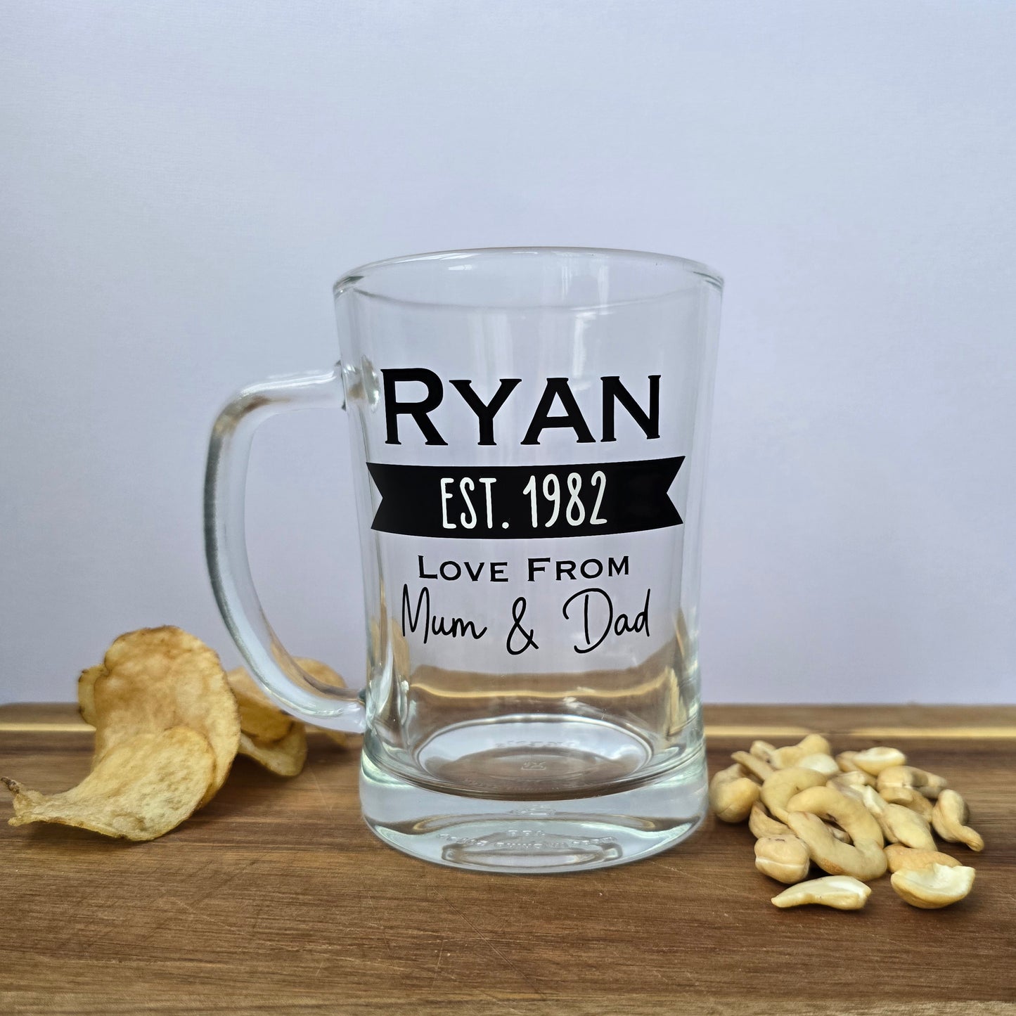 Glass beer tankard personalised with a name, year and signed from the gift giver in black vinyl on clear glass. Sturdy, heavy, clear glass stein with mixed font design. 