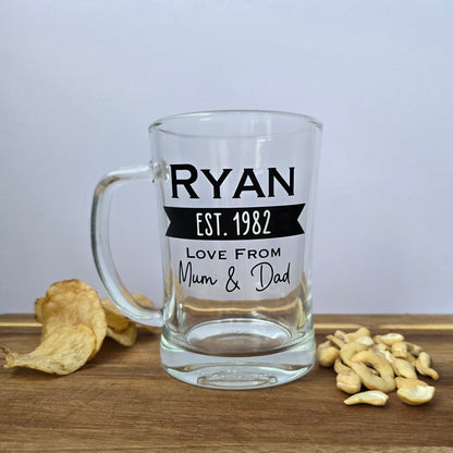 Glass beer tankard personalised with a name, year and signed from the gift giver in black vinyl on clear glass. Sturdy, heavy, clear glass stein with mixed font design. 