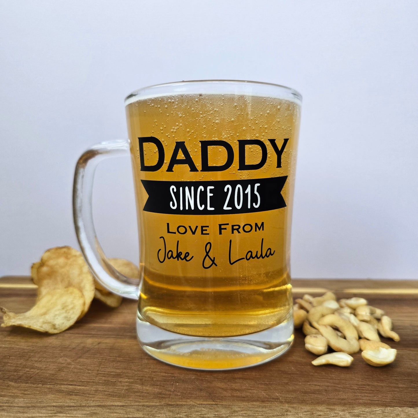 Glass beer tankard personalised with a name, year and signed from the gift giver in black vinyl on clear glass. Sturdy, heavy, clear glass stein with mixed font design. 