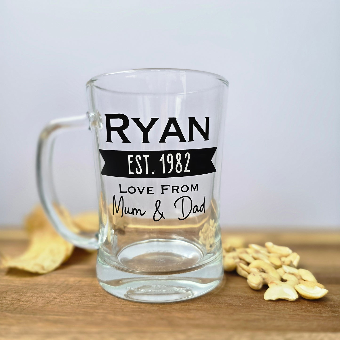 Glass beer tankard personalised with a name, year and signed from the gift giver in black vinyl on clear glass. Sturdy, heavy, clear glass stein with mixed font design. 
