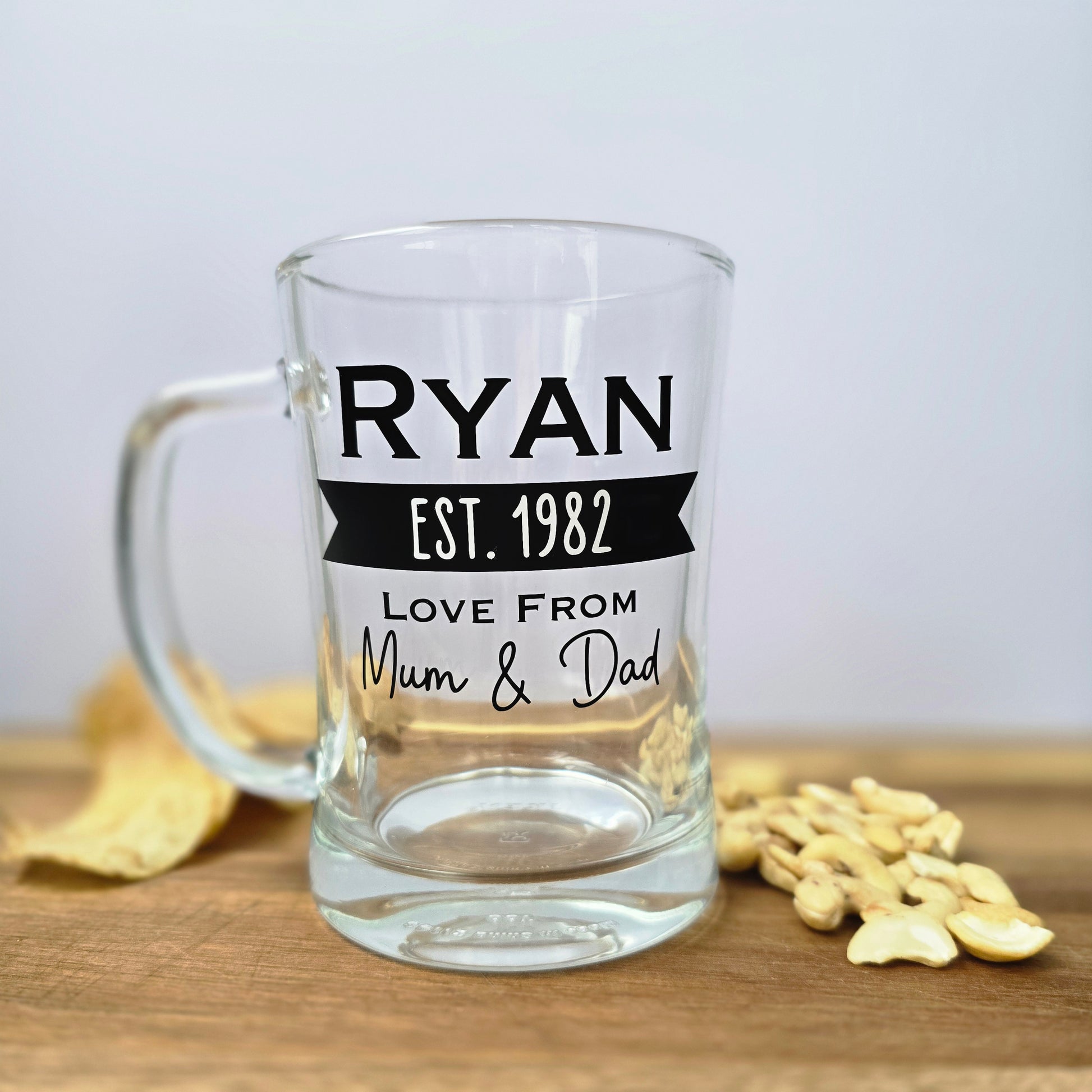 Glass beer tankard personalised with a name, year and signed from the gift giver in black vinyl on clear glass. Sturdy, heavy, clear glass stein with mixed font design. 