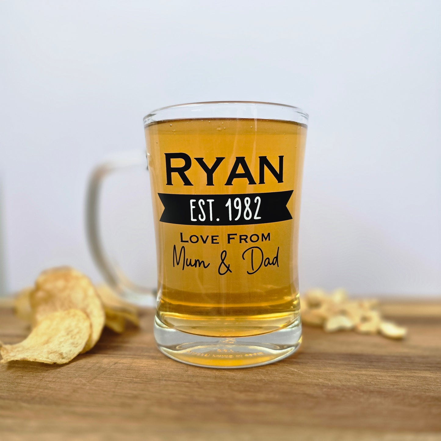 Glass beer tankard personalised with a name, year and signed from the gift giver in black vinyl on clear glass. Sturdy, heavy, clear glass stein with mixed font design. 