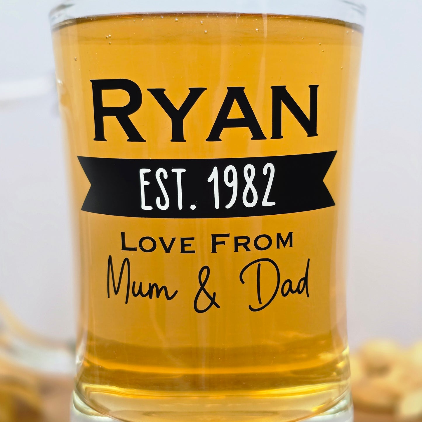 Glass beer tankard personalised with a name, year and signed from the gift giver in black vinyl on clear glass. Sturdy, heavy, clear glass stein with mixed font design. 