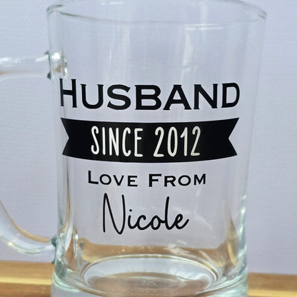Glass beer tankard personalised with a name, year and signed from the gift giver in black vinyl on clear glass. Sturdy, heavy, clear glass stein with mixed font design. 