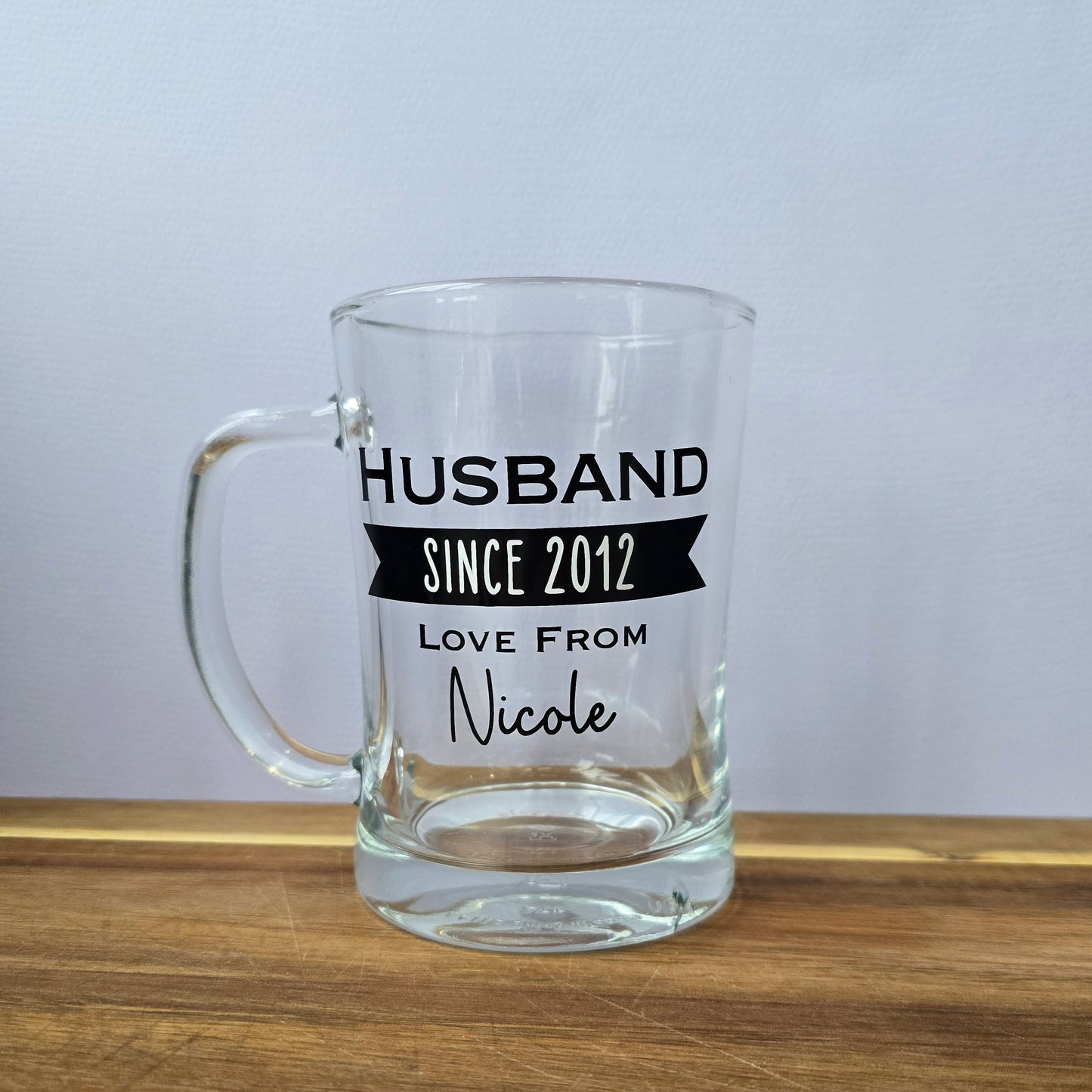 Glass beer tankard personalised with a name, year and signed from the gift giver in black vinyl on clear glass. Sturdy, heavy, clear glass stein with mixed font design. 