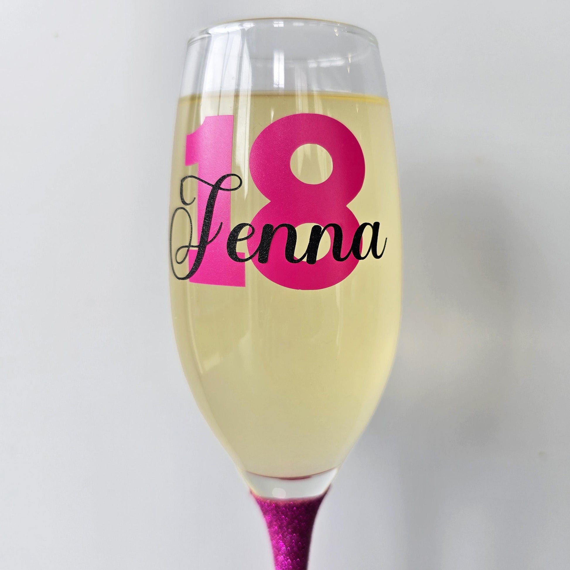 Personalised champagne flute or prosecco glass with glitter stem and with a birthday age number in block, glitter or metallic vinyl and a name in black decorative font through the number