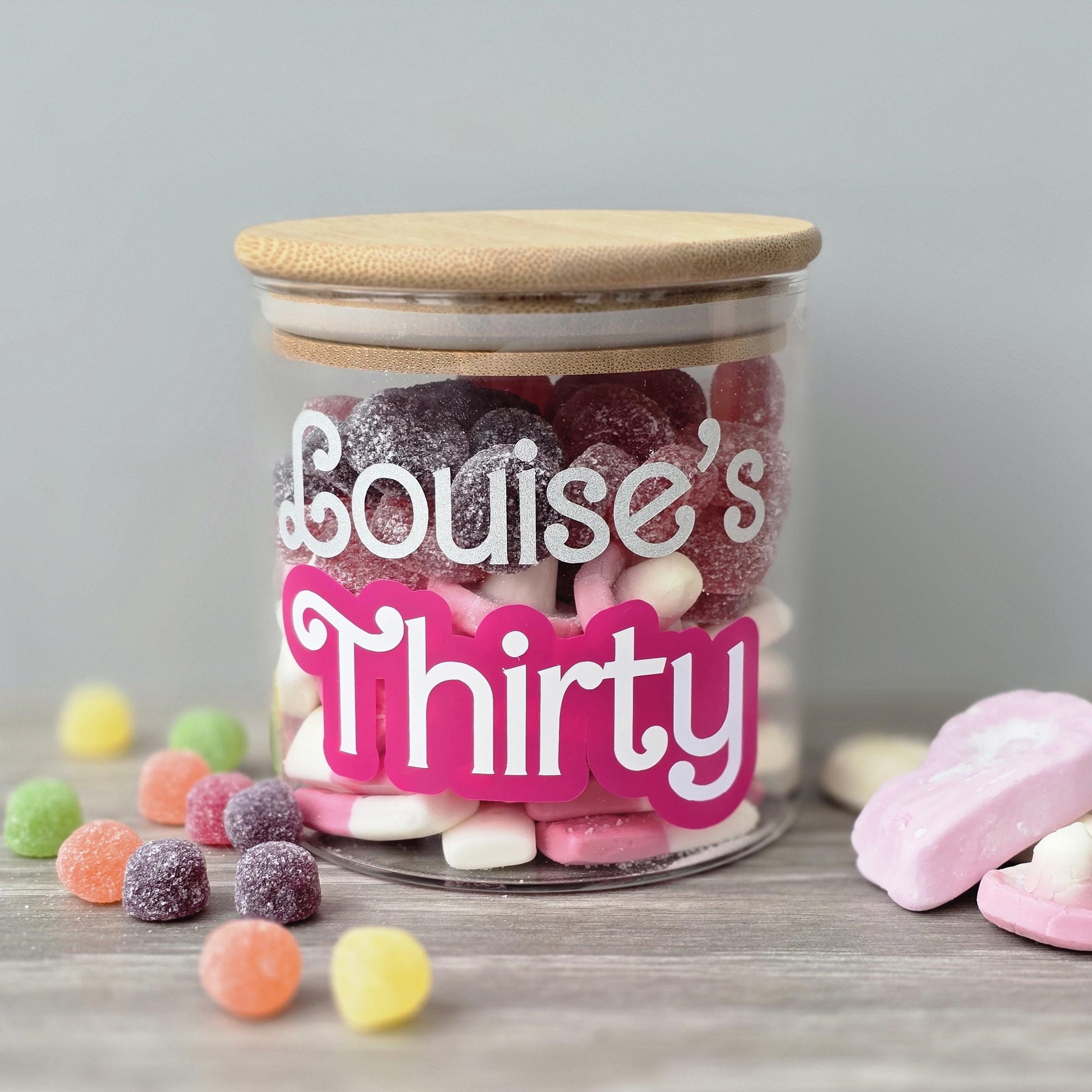 Jar of colorful candies with 'Louise's Thirty' label on a wooden surface.
