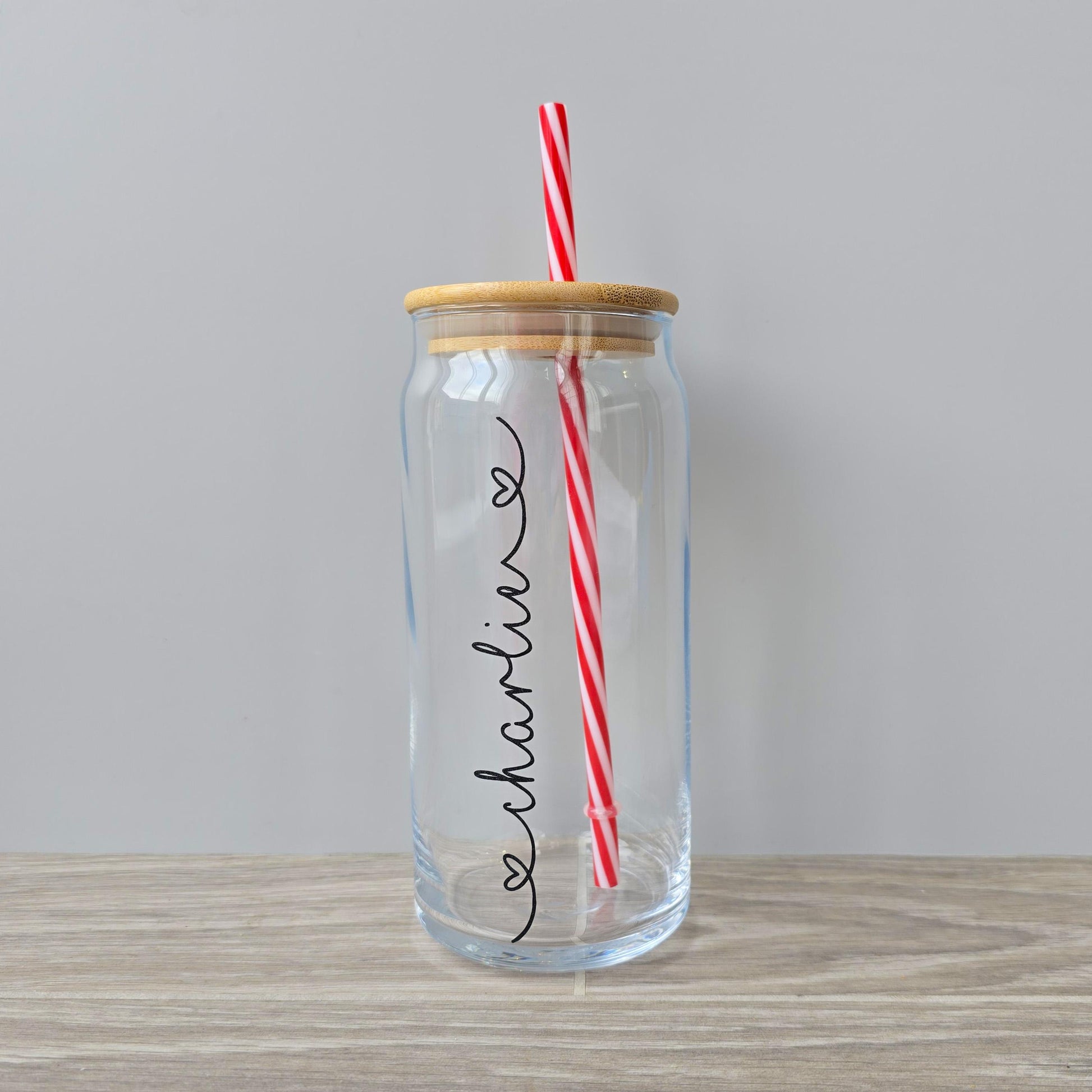 Personalised glass can drink tumbler with a bamboo suction lid and red and white reusable straw. Name printed in decorative font, in a range of colours, printed along the glass.