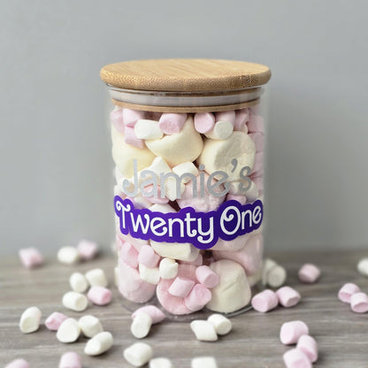 Jar of colorful candies with a wooden lid and 'Jamie's Twenty One' label on a gray background.