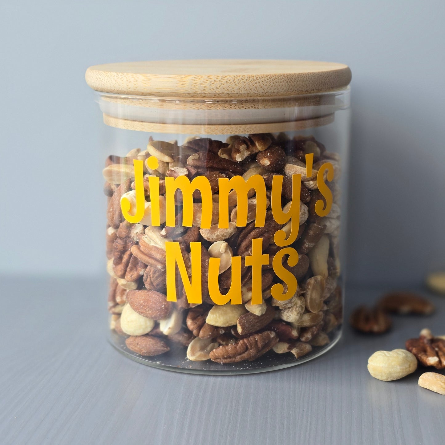 Personalised glass jar with wooden suction lids, mixed nuts 'Jimmy's Nuts' label on a grey background