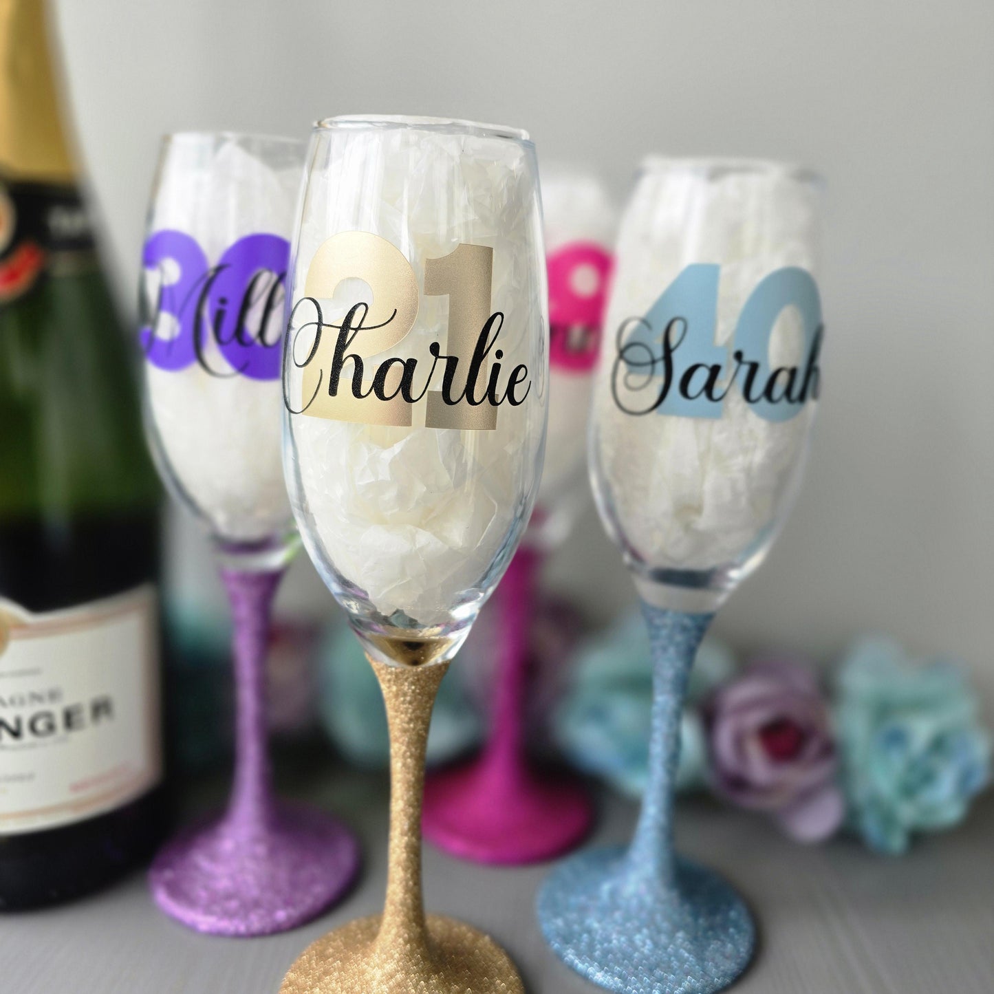 Personalised champagne flute or prosecco glass with glitter stem and with a birthday age number in block, glitter or metallic vinyl and a name in black decorative font through the number