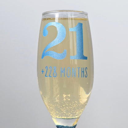 Prosecco glass or Champagne flute decorated with high shine glitter stem and personalised with 21 + the number of months to make up a 30th, 40th, 50th, 60th or 70th Birthday.