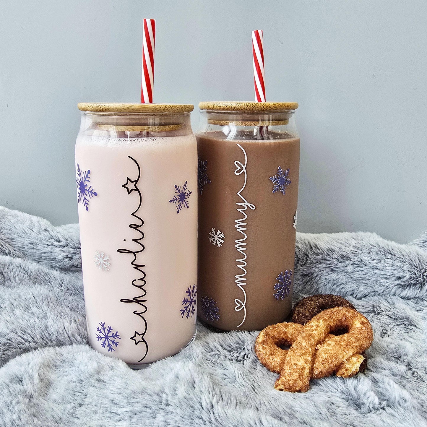 Personalised glass can drink holder with a bamboo suction lid and red and white reusable straw. Features silver snowflakes and blue snowflakes that colour change to purple when cold liquid is added to the glass. Personalised name along the side of the glass, available in glittery silver or black and features either a heart or stars at either end of the name.