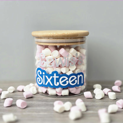 Glass Jar with airtight suction lid with pink and white heart-shaped marshmallows, personlised with a name and with a 'Sixteen' label on a wooden surface.