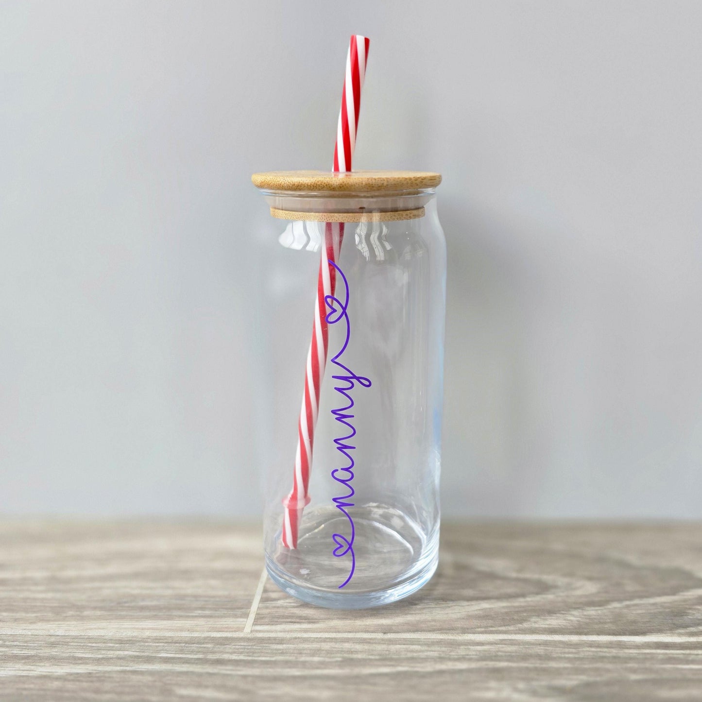 Personalised glass can drink tumbler with a bamboo suction lid and red and white reusable straw. Name printed in decorative font, in a range of colours, printed along the glass.