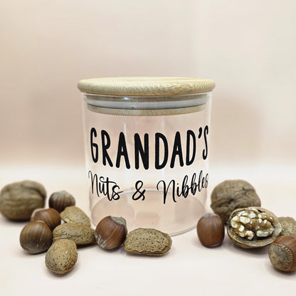 Jar labeled 'Grandad's Nuts & Nibbles' surrounded by nuts on a light background