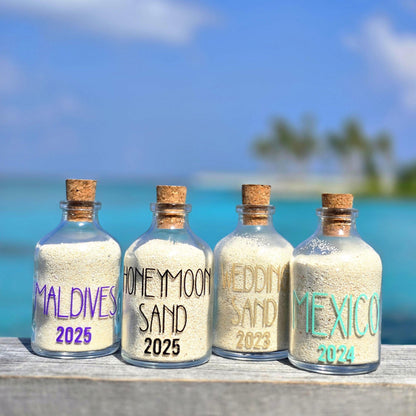 Four bottles with cork lids containing sand from different locations with beach background
