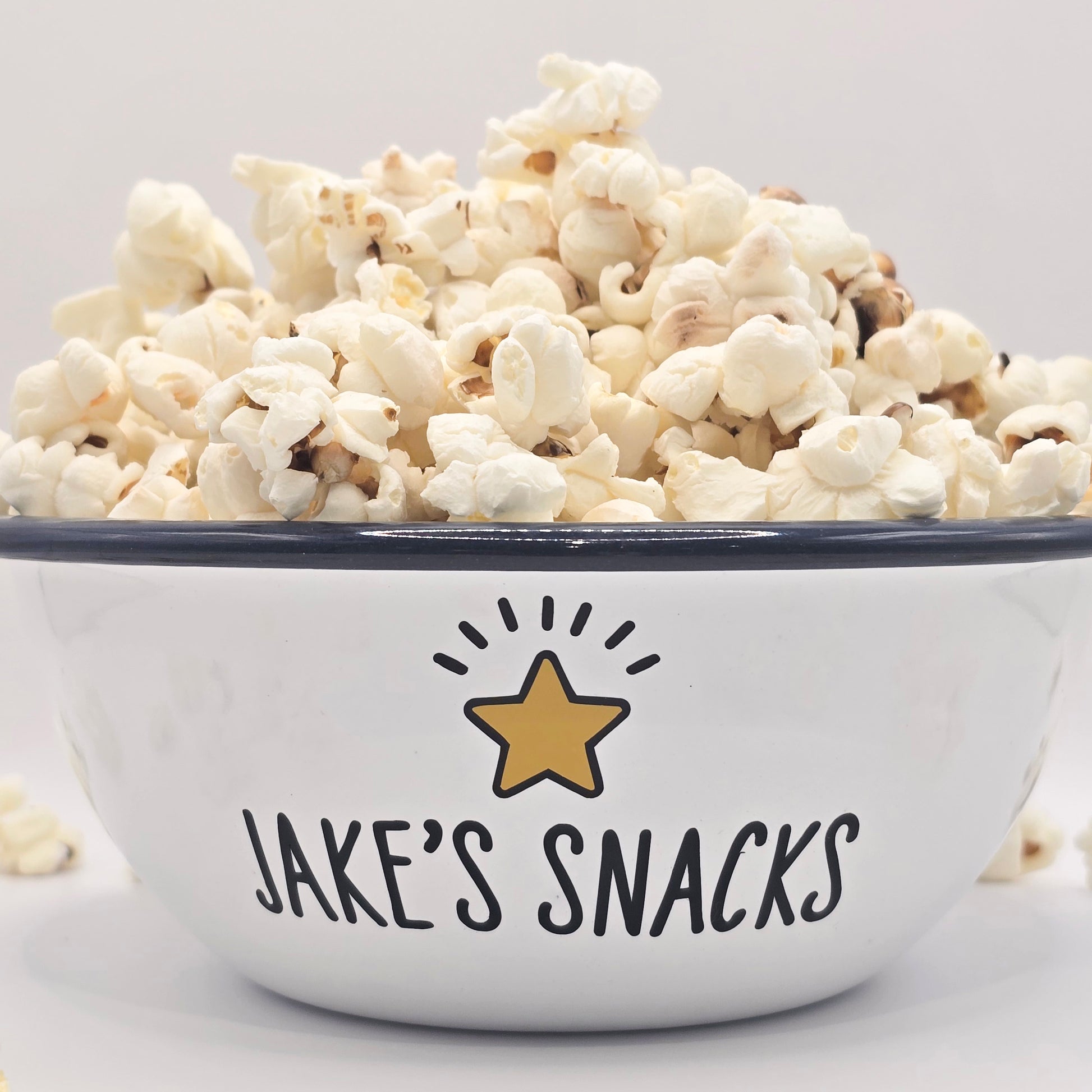 Kids Personalised white metal enamel snack bowl. White enamel metal bowl with navy blue rim. Printed with a yellow star or red heart and a name with snacks written underneath. Perfect for popcorn, sweets, crisps or general snacks.