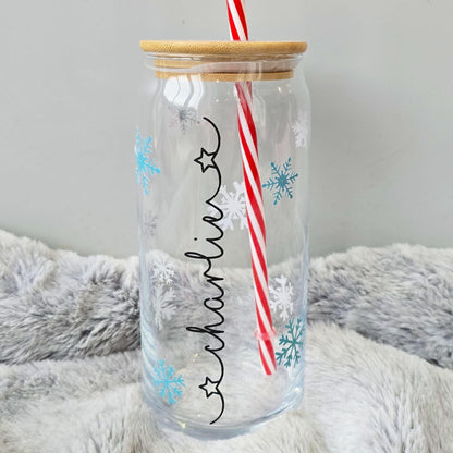 Personalised glass can drink holder with a bamboo suction lid and red and white reusable straw. Features silver snowflakes and blue snowflakes that colour change to purple when cold liquid is added to the glass. Personalised name along the side of the glass, available in glittery silver or black and features either a heart or stars at either end of the name.