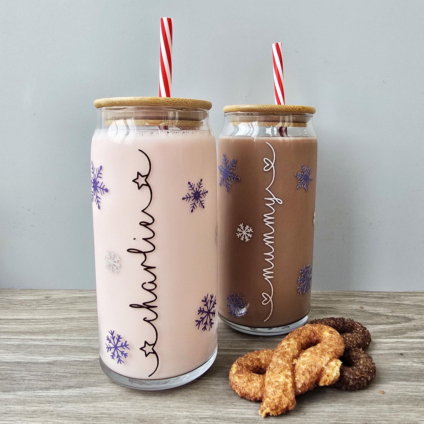 Personalised glass can drink holder with a bamboo suction lid and red and white reusable straw. Features silver snowflakes and blue snowflakes that colour change to purple when cold liquid is added to the glass. Personalised name along the side of the glass, available in glittery silver or black and features either a heart or stars at either end of the name.