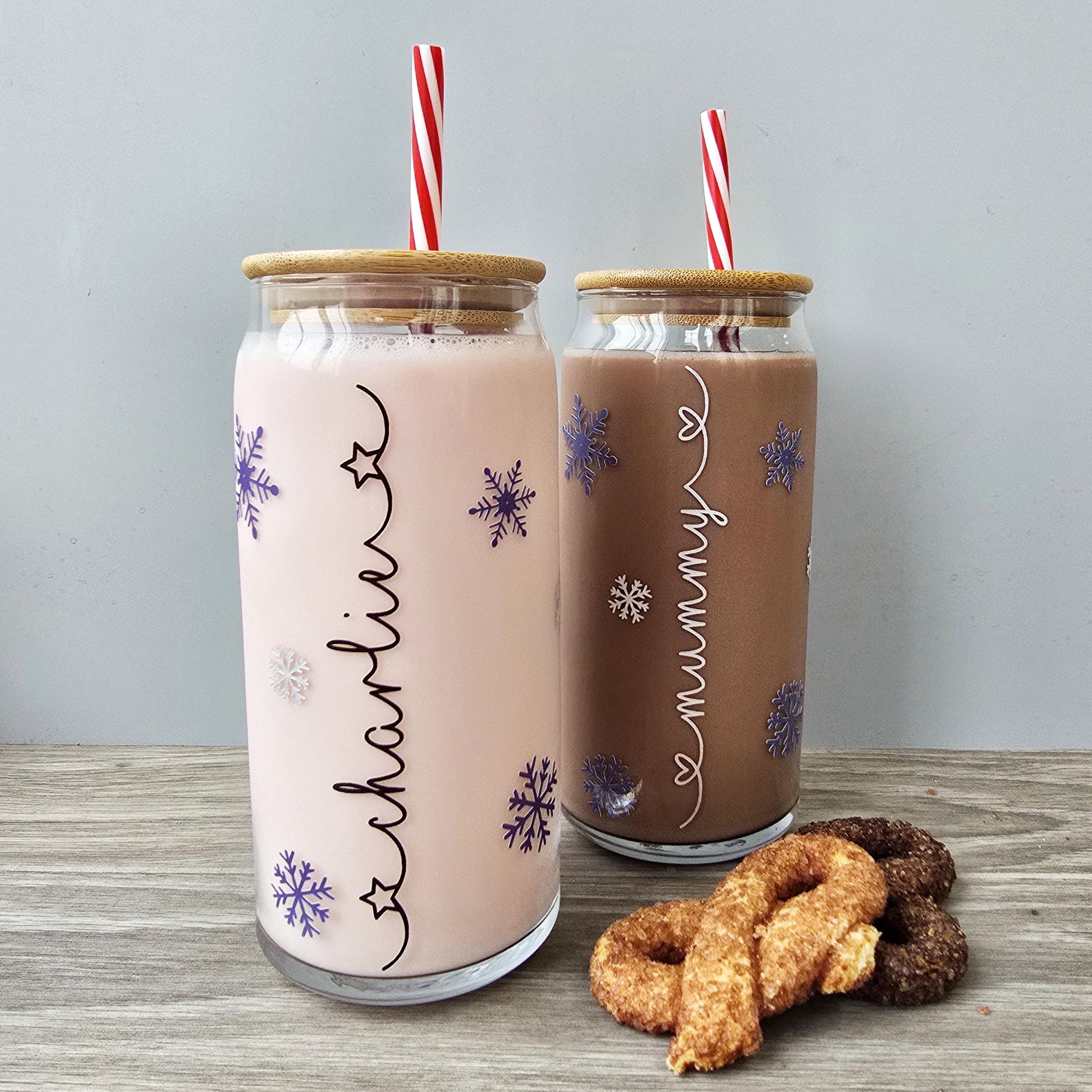 Personalised glass can drink holder with a bamboo suction lid and red and white reusable straw. Features silver snowflakes and blue snowflakes that colour change to purple when cold liquid is added to the glass. Personalised name along the side of the glass, available in glittery silver or black and features either a heart or stars at either end of the name.