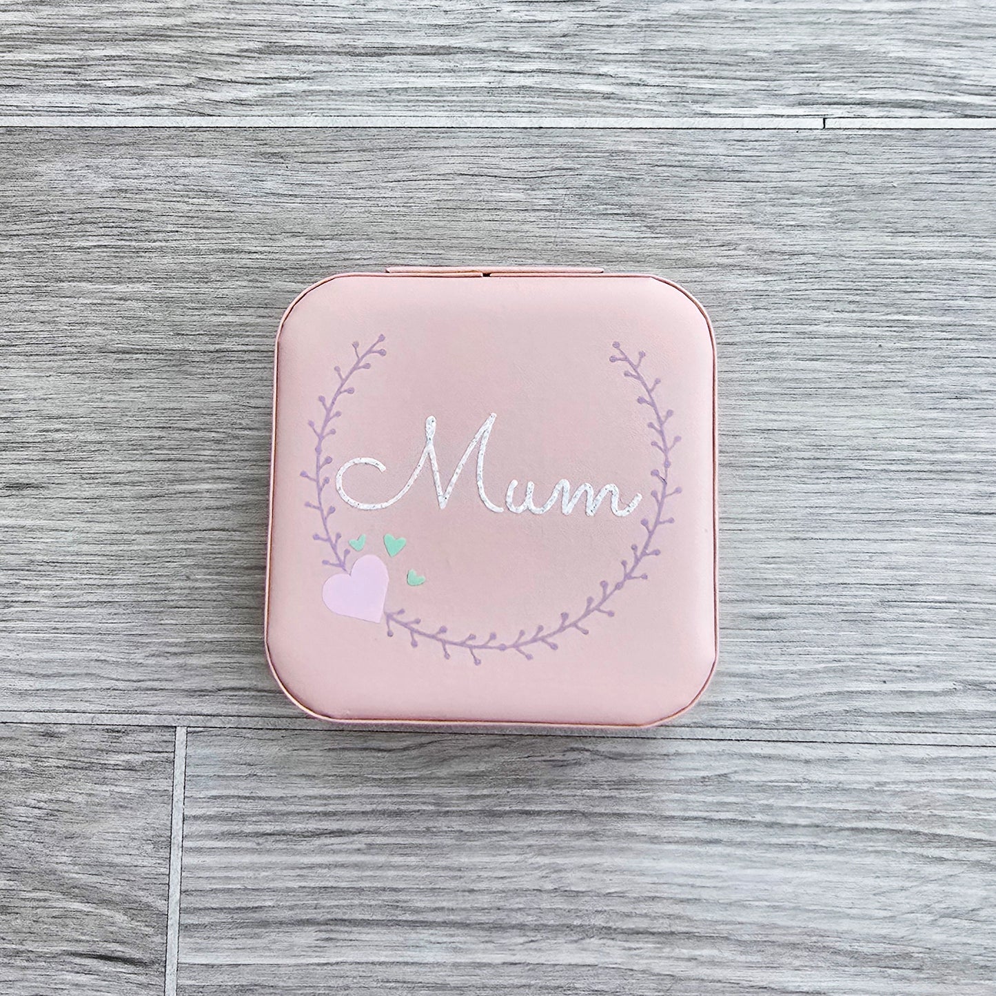 Faux leather, travel jewellery box personalised with a name in the middle of a decorative circle, decorated with hearts. Travel size jewellery case with zip and internal jewellery dividers.