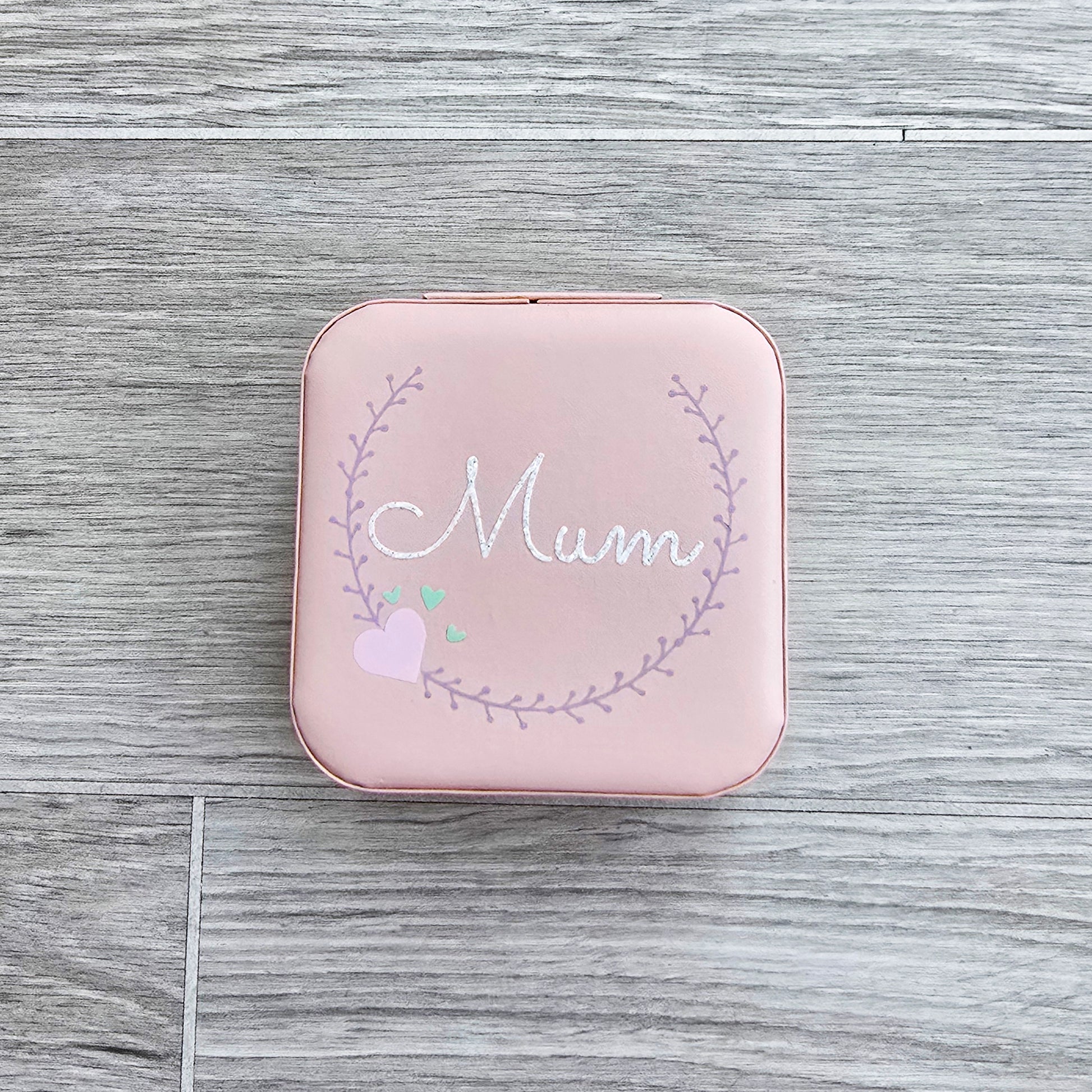 Faux leather, travel jewellery box personalised with a name in the middle of a decorative circle, decorated with hearts. Travel size jewellery case with zip and internal jewellery dividers.