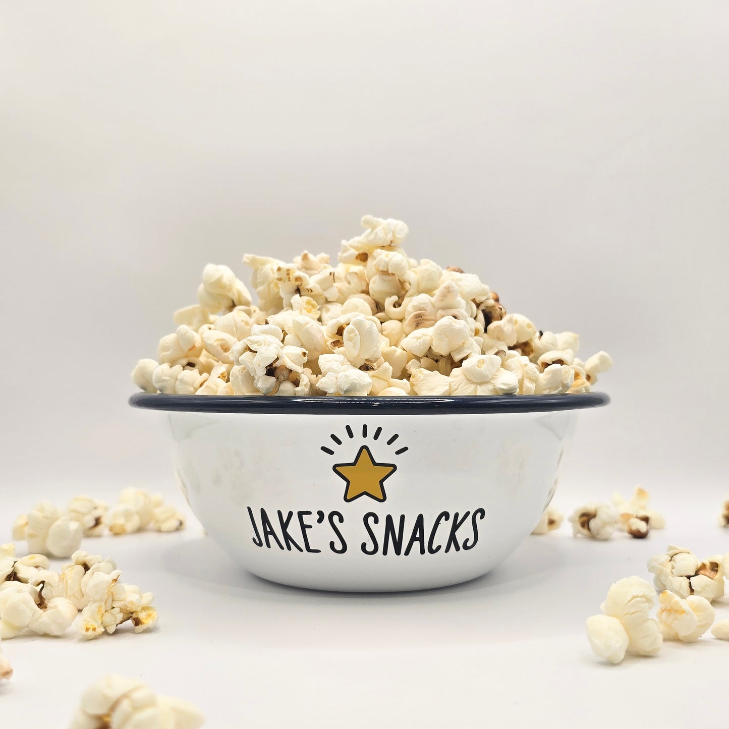 Kids Personalised white metal enamel snack bowl. White enamel metal bowl with navy blue rim. Printed with a yellow star or red heart and a name with snacks written underneath. Perfect for popcorn, sweets, crisps or general snacks.