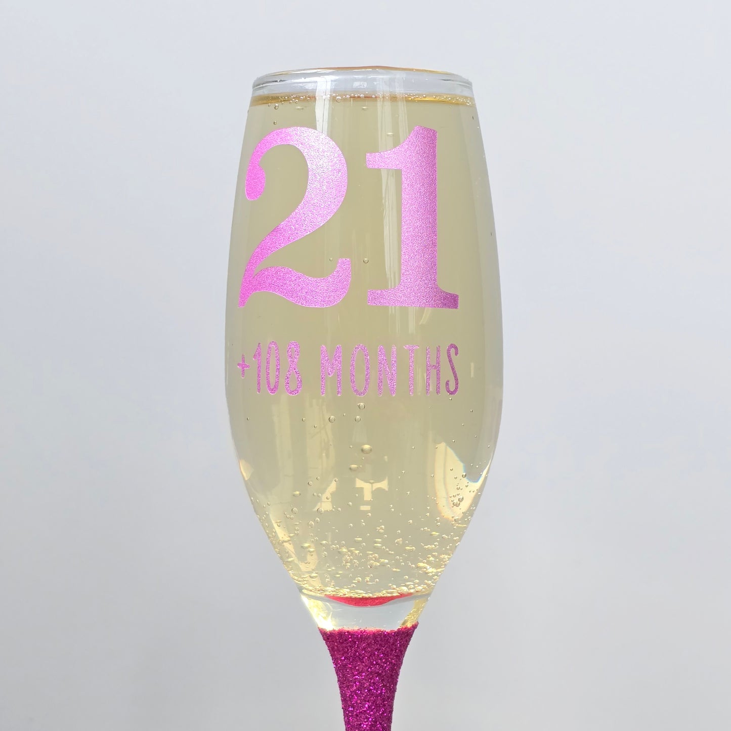 Prosecco glass or Champagne flute decorated with high shine glitter stem and personalised with 21 + the number of months to make up a 30th, 40th, 50th, 60th or 70th Birthday.