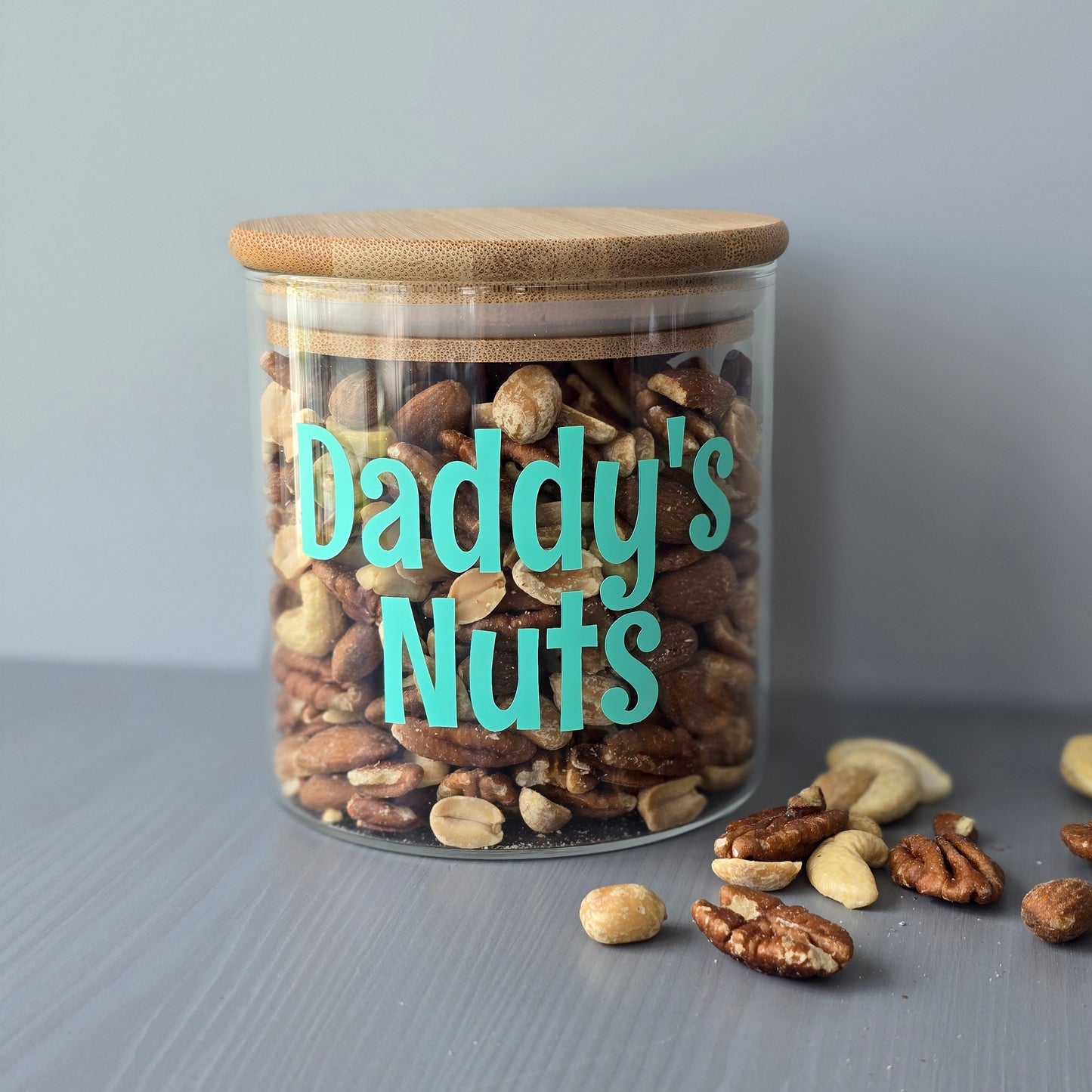 Personalised glass jar with wooden suction lids, with mixed nuts with 'Daddy's Nuts' label on a grey surface