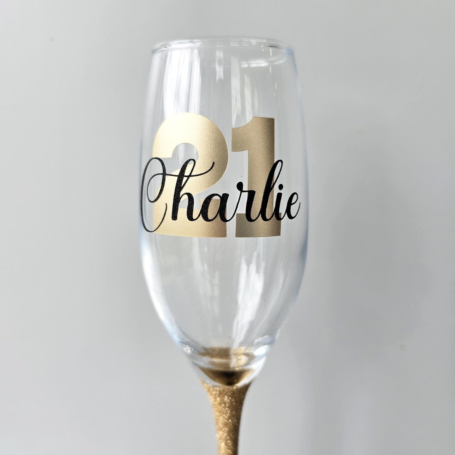 Personalised champagne flute or prosecco glass with glitter stem and with a birthday age number in block, glitter or metallic vinyl and a name in black decorative font through the number