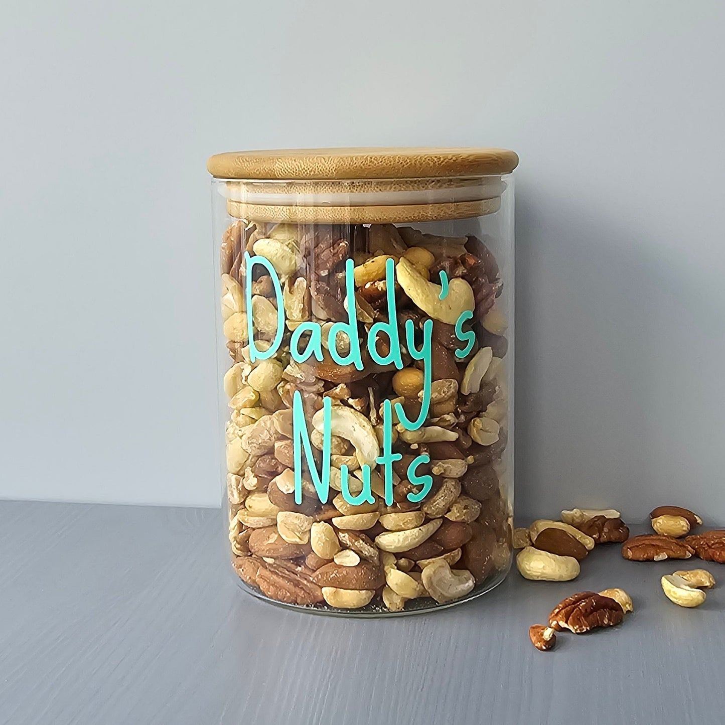 Personalised glass jar with wooden suction lids, filled with mixed nuts labeled 'Daddy's Nuts' on a grey background