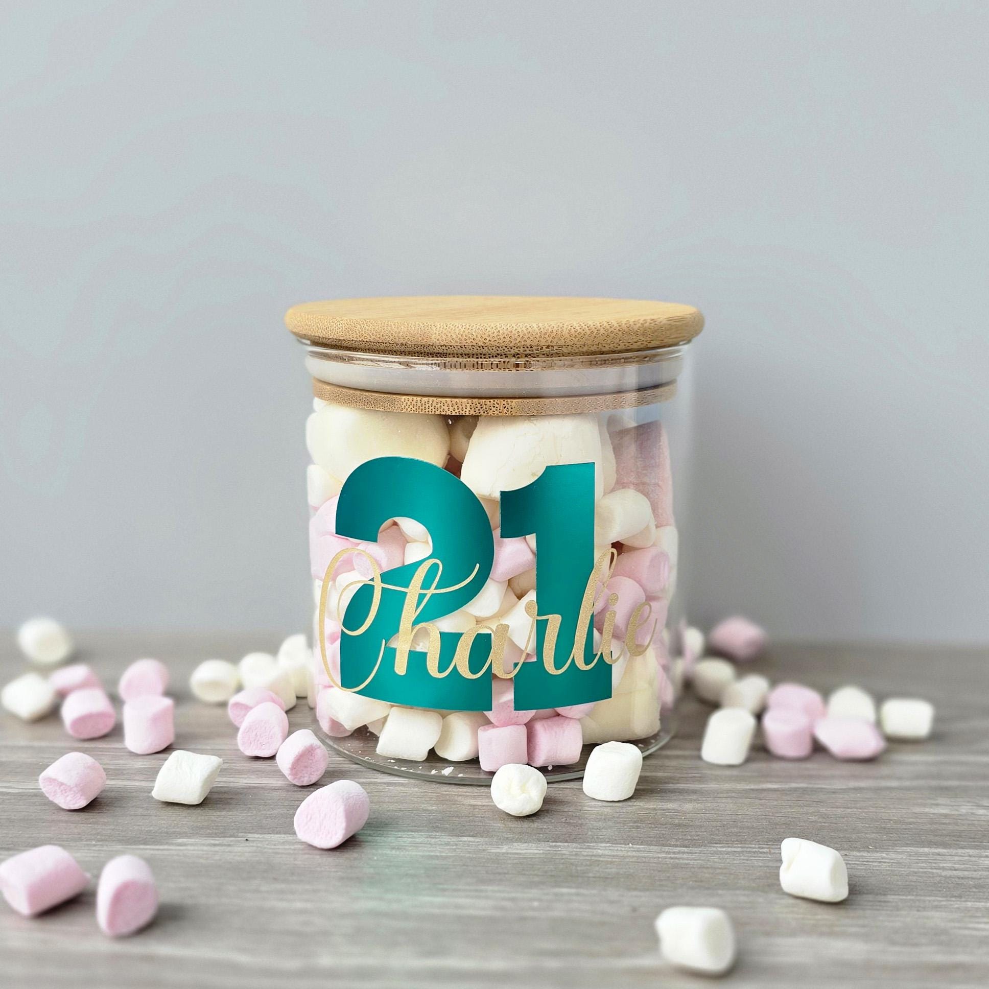 Glass jar with wooden lid filled with colorful candies on a gray surface.