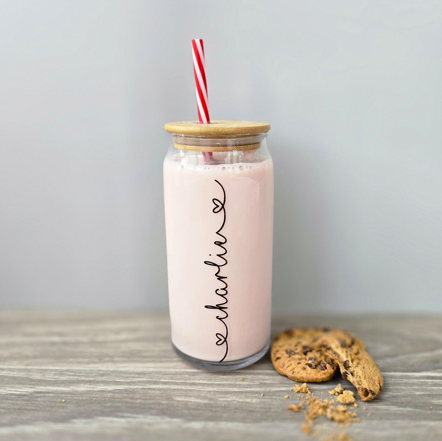 Personalised glass can drink tumbler with a bamboo suction lid and red and white reusable straw. Name printed in decorative font, in a range of colours, printed along the glass.
